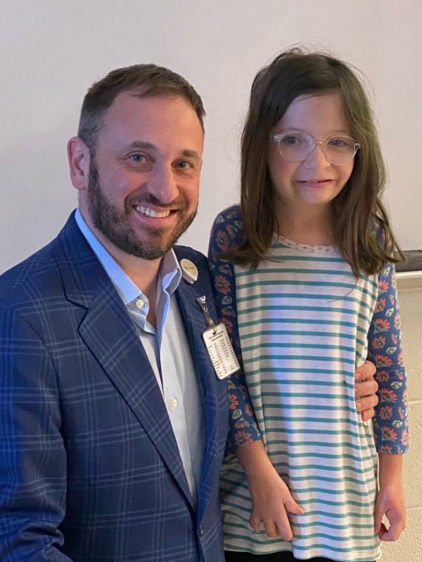 A young girl after treatment for craniosynostosis standing with the doctor.